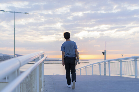 Junger chinesischer Mann mit Skateboard am Strand bei Sonnenaufgang, lizenzfreies Stockfoto