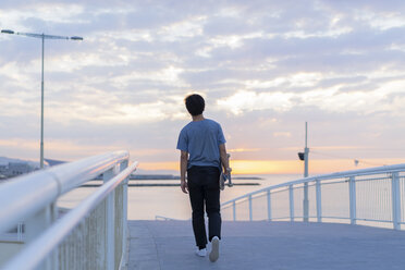 Junger chinesischer Mann mit Skateboard am Strand bei Sonnenaufgang - AFVF00716
