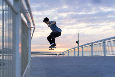 Junger chinesischer Mann auf dem Skateboard bei Sonnenaufgang am Strand - AFVF00717