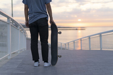 Junger Mann mit Skateboard am Strand bei Sonnenaufgang, Rückansicht - AFVF00719