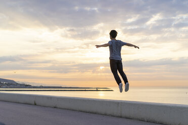 Junger chinesischer Mann springt am Strand auf eine Mauer - AFVF00726