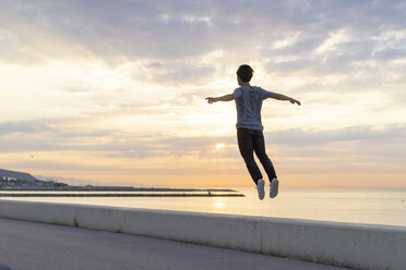 Young Chinese man jumping on wall at the beach - AFVF00726