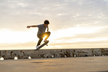 Young Chinese man skateboarding at sunsrise near the beach - AFVF00733
