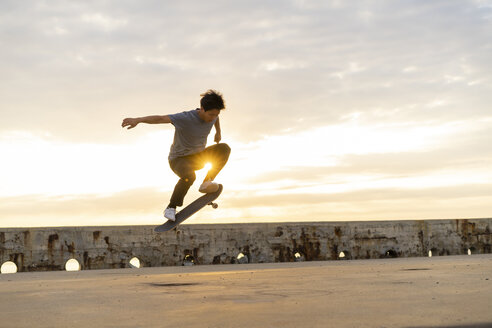 Junger chinesischer Mann auf dem Skateboard bei Sonnenaufgang am Strand - AFVF00733