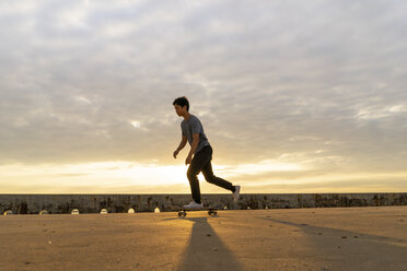 Junger chinesischer Mann auf dem Skateboard bei Sonnenaufgang am Strand - AFVF00734