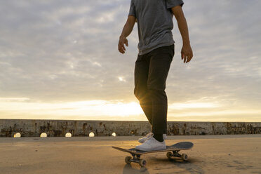 Junger chinesischer Mann auf dem Skateboard bei Sonnenaufgang am Strand - AFVF00735