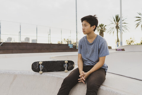 Junger chinesischer Mann sitzt auf der Mauer eines Skateparks in der Nähe des Strandes, lizenzfreies Stockfoto
