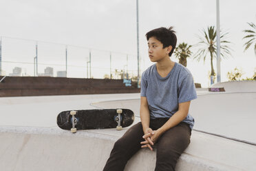 Junger chinesischer Mann sitzt auf der Mauer eines Skateparks in der Nähe des Strandes - AFVF00738