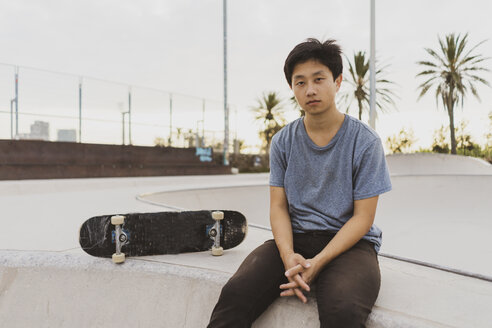 Junger chinesischer Mann sitzt auf der Mauer eines Skateparks in der Nähe des Strandes - AFVF00739