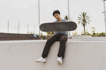 Junger chinesischer Mann sitzt auf der Mauer eines Skateparks in der Nähe des Strandes - AFVF00740