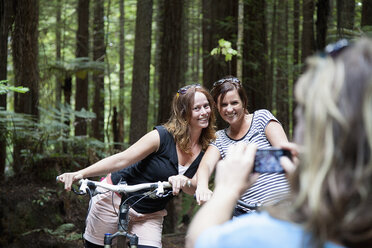 Blick über die Schulter von Mountainbikerinnen, die mit ihrem Smartphone im Wald für ein Foto posieren - ISF16669