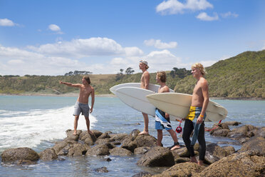 Four young male surfer friends pointing to sea from rocks - ISF16730