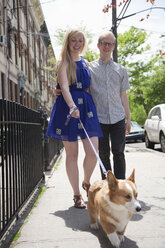 Junges Paar geht mit Corgi-Hund auf der Straße spazieren - ISF16747