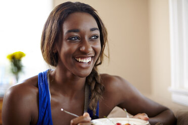 Young woman on a training break, eating fruit in sitting room - ISF16782