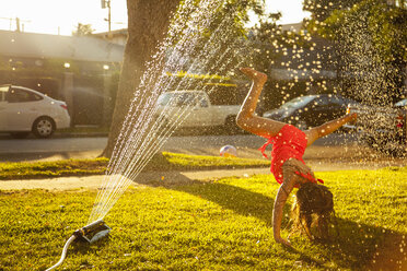 Girl doing handstand under in garden sprinkler - ISF16791