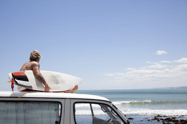 Mature male surfer watching from vehicle roof at beach - ISF16795