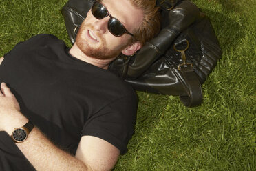 Man laying on bag in grass - CUF39728