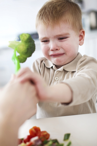 Weinender Junge verweigert Brokkoli in der Küche, lizenzfreies Stockfoto