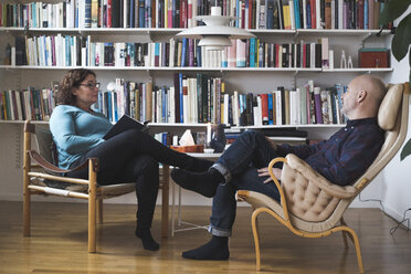 Mature female therapist talking to patient by bookshelf at home office - MASF08009