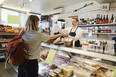 Male sales clerk holding plastic bag while accepting credit card from customer at checkout counter - MASF08015