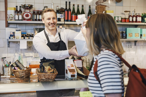 Männlicher Verkäufer lächelt, während er einem Kunden an der Ladentheke eine Tasche überreicht - MASF08023