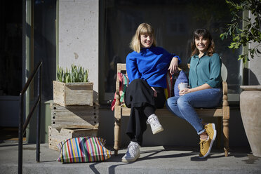 Full length portrait of smiling owners sitting on bench outside store - MASF08050