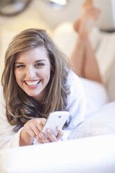 Portrait of young woman lying on bed with mobile phone - CUF39783