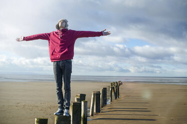 Young man standing on groynes, Brean Sands, Somerset, England - CUF39876
