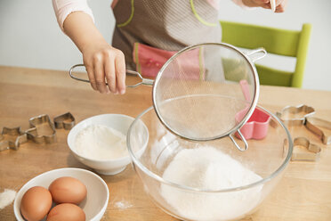 Girl sieving flour into mixing bowl - CUF39904