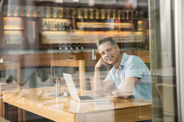 Businessman using laptop, view through window - CUF39948