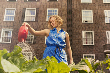 Young woman watering vegetables on council estate allotment - CUF39955