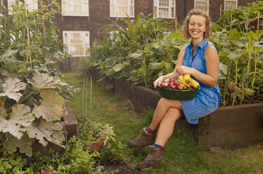 Junge Frau mit geerntetem Gemüse in einer Kleingartensiedlung - CUF39958