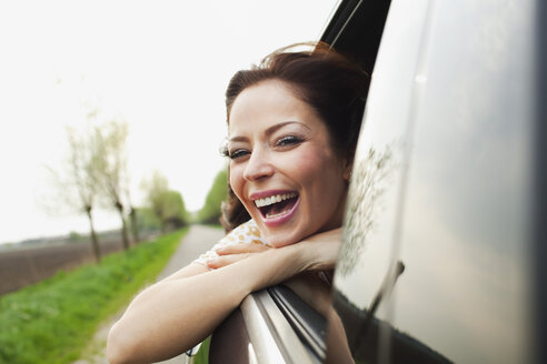 Junge Frau lehnt sich lachend aus dem Autofenster - CUF40040