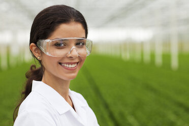 Scientist wearing goggles in front of plants in greenhouse - CUF40044