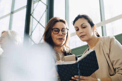 Geschäftsfrauen diskutieren über den Terminkalender, während sie ein Smartphone bei einer Bürobesprechung benutzen - MASF08094