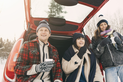 Niedriger Blickwinkel auf glückliche Freunde, die im Winter im Kofferraum eines Autos Kaffee trinken und sich ausruhen, lizenzfreies Stockfoto