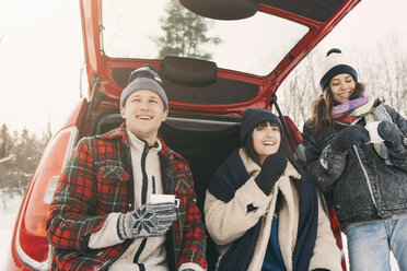 Niedriger Blickwinkel auf glückliche Freunde, die im Winter im Kofferraum eines Autos Kaffee trinken und sich ausruhen - MASF08105