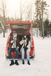 Freunde in voller Länge beim Kaffeetrinken im Kofferraum eines Autos auf einer verschneiten Wiese - MASF08107