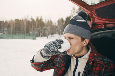 Man drinking coffee in car trunk at park during winter - MASF08110