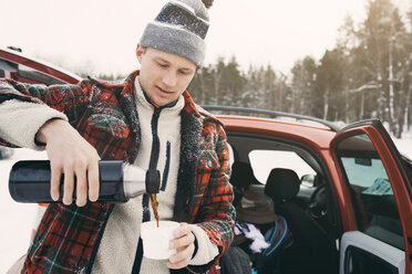 Mid adult man pouring coffee from insulated drink container while standing by car - MASF08115