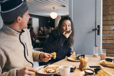 Frau isst Frühstück und sitzt mit einem Freund am Tisch in einer Blockhütte - MASF08121