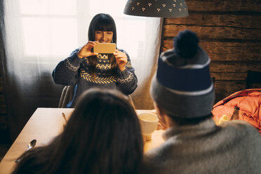 Frau fotografiert Freunde mit dem Mobiltelefon, während sie in einer Blockhütte sitzt - MASF08123