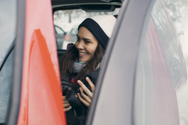 Lächelnde mittelgroße erwachsene Frau im Auto sitzend, gesehen durch die offene Tür - MASF08132