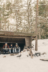 Freunde sitzen im Winter in einer Blockhütte vor Bäumen - MASF08136