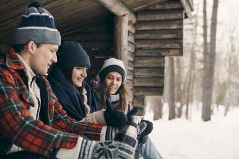 Mann gibt seinen Freundinnen etwas zu trinken, während er im Winter in einer Blockhütte sitzt, lizenzfreies Stockfoto