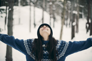 Happy woman standing with arms raised on snowy field during winter - MASF08143