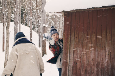 Mann wirft Schneeball, während er mit einem Freund bei einer Blockhütte im Winter steht - MASF08146