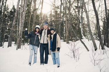 Lächelnde Freunde in voller Länge auf einem schneebedeckten Feld gegen Bäume stehend - MASF08155