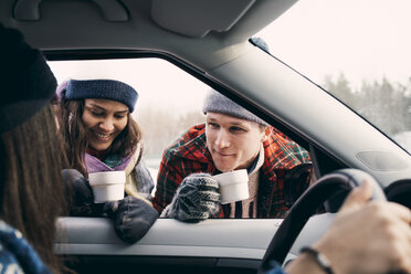 Lächelnder Mann und Frau im Gespräch mit einem Freund im Auto sitzend beim Kaffee trinken im Winter - MASF08161