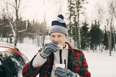 Man eating bread while having coffee in car trunk at park during winter - MASF08163